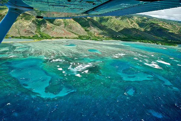 Reflection in wing of Cessna 172.  Flying south side of Molokai, Hawaii.  Vivid blues and greens in water.