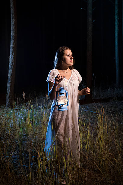 istock lost woman in forest at night walking with candle lantern 480211734