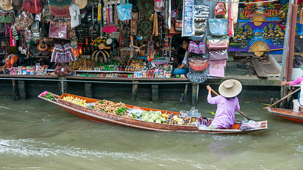Damnoen Saduak Floating Market In Thailand Damnoen Saduak, Thailand - July 22, 2011: A woman selling fruit from her boat at Damnoen Saduak floating market in Thailand. The Market is held everyday until noon and has become very popular with tourists. ratchaburi province stock pictures, royalty-free photos & images