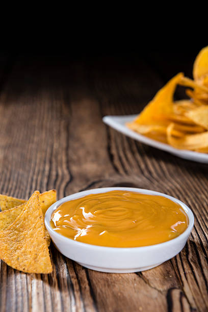 Nachos with Cheese Dip Nachos with Cheese Dip (close-up shot) on an wooden table cheese sauce stock pictures, royalty-free photos & images