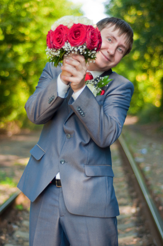 the beautiful young groom with a bouquet of red-white roses on a track in the summer