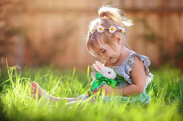 Photo of Little girl playing with a bunny on the grass