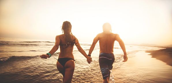Silhouette of couple in love running on the beach and holding hands.