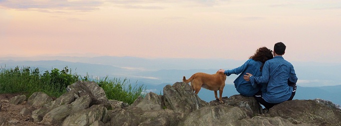 Couple resting on mountain top with dog at sunrise looking at view in North Carolina,