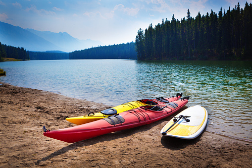Water sport of paddle boarding, kayaking on the  scenic Johnson Lake in Banff National Park of Canada. Two kayaks and a paddle board on the beach of Lake Johnson. Banff National Park in the Canadian Rockies, a popular tourist destination and vacationers, offers a variety of water sport actives. Photographed on location in horizontal format.