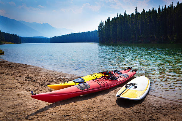 Kayaks Paddle Board in Johnson Lakes of Banff National Park Water sport of paddle boarding, kayaking on the  scenic Johnson Lake in Banff National Park of Canada. Two kayaks and a paddle board on the beach of Lake Johnson. Banff National Park in the Canadian Rockies, a popular tourist destination and vacationers, offers a variety of water sport actives. Photographed on location in horizontal format. paddleboard photos stock pictures, royalty-free photos & images