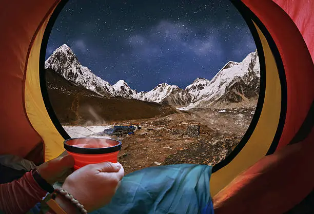 Woman lying in a tent with coffee ,view of mountains and sky in Gorak Shep village - Nepal, Himalayas