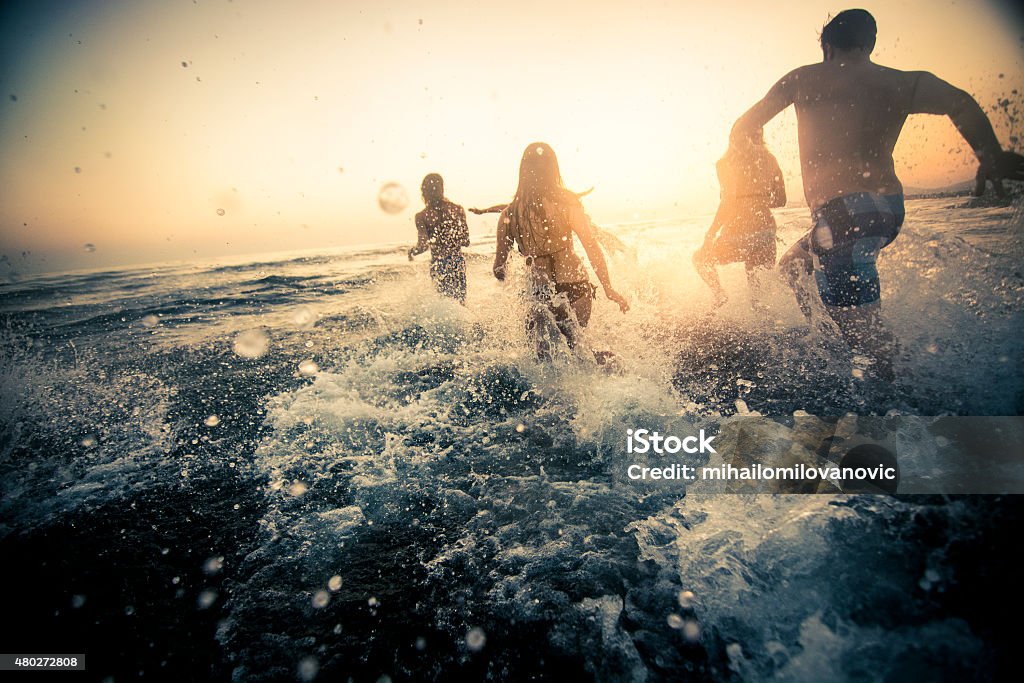 Group of friends running into the water Group of friends running in the ocean at sunset and having fun Beach Stock Photo