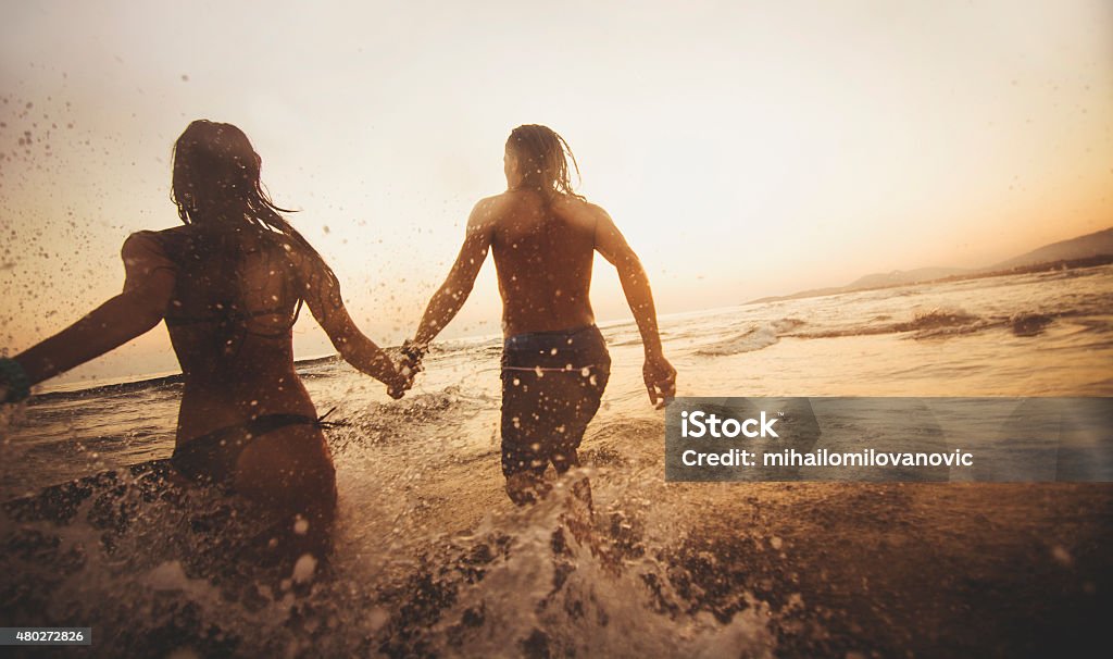 Couple running in the water Silhouette of couple in love running on the beach and holding hands. Sport Stock Photo