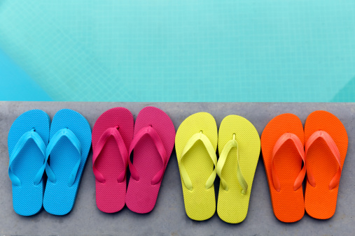 Row of colorful flip flops on grey stone at the pools' edge. Space for copy.