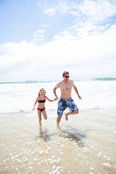 istock Happy father and daughter running from waves at beach 480296719