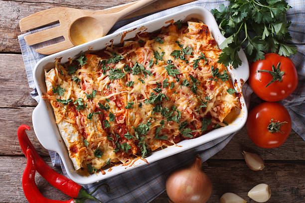 Mexican enchilada in a baking dish horizontal top view close-up Mexican enchilada in a baking dish with the ingredients on the table close-up. horizontal view from above omelet rustic food food and drink stock pictures, royalty-free photos & images