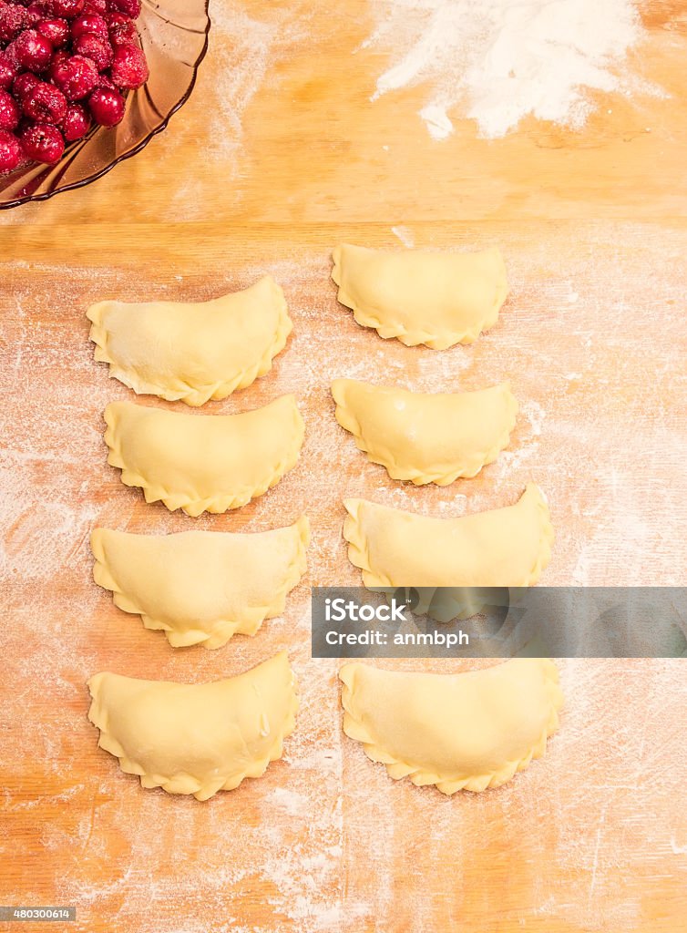 Making dumplings Making ukrainian varenyky (dumplings) filled with sour cherry with sugar on a wood cutting board 2015 Stock Photo