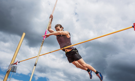 Low angle view of a young man making an effort at pole vault competition.