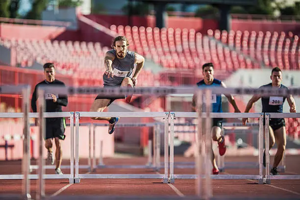 Four young man jumping hurdles on a sports race at stadium.