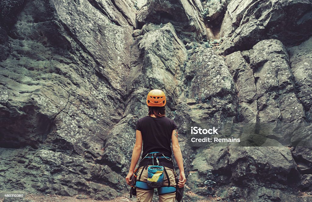 Climber woman standing in front of a stone rock outdoor Young woman wearing in climbing equipment standing in front of a stone rock outdoor and preparing to climb, rear view Rock Climbing Stock Photo