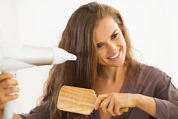 happy young woman brushing and blow drying hair in bathroom Happy young woman brushing and blow drying hair in bathroom fen photos stock pictures, royalty-free photos & images