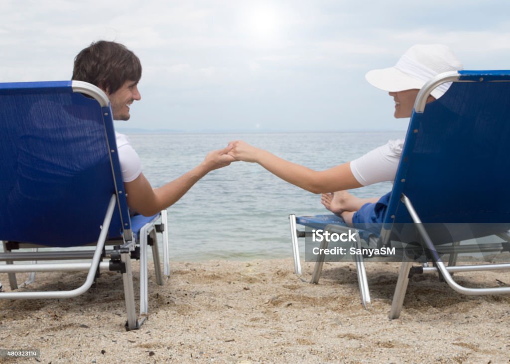 Couple on a beach Young couple is sitting on a beach. Chairs are blue. They are looking at sunset and holding hands. 2015 Stock Photo