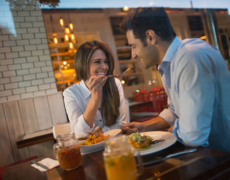 Happy Latin American couple having a romantic dinner at a restaurant and woman feeding her man