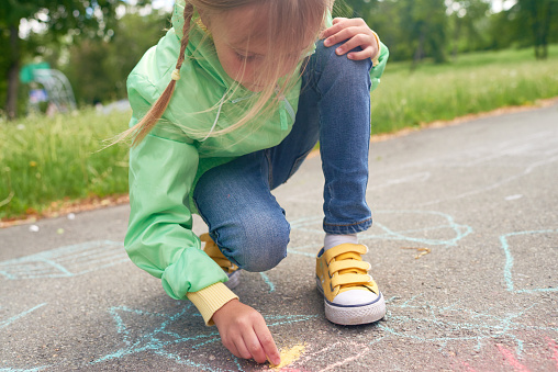 Lovely little girl drawing with sidewalk chalk on asphalt
