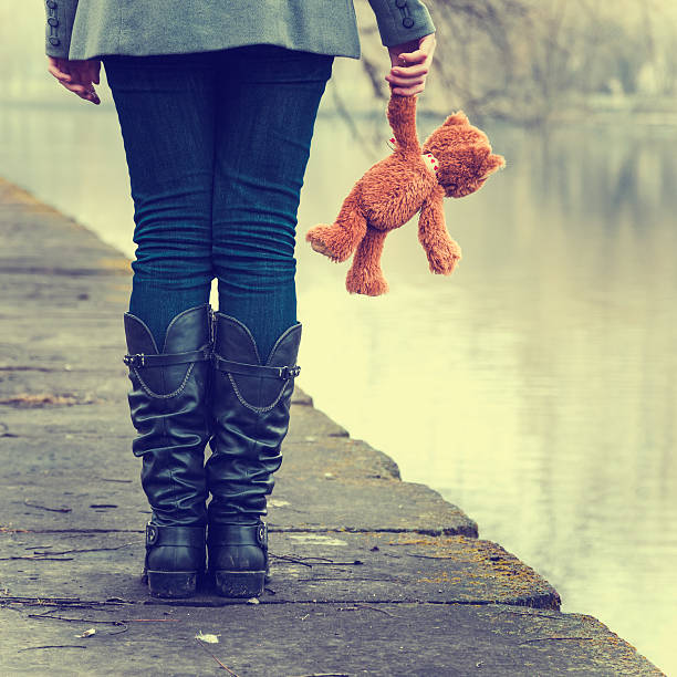 Sad lonely girl with teddy bear near river