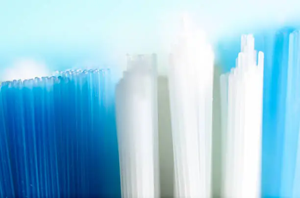 Close-up Macro picture of Blue and White Toothbrush bristles on light blue background.