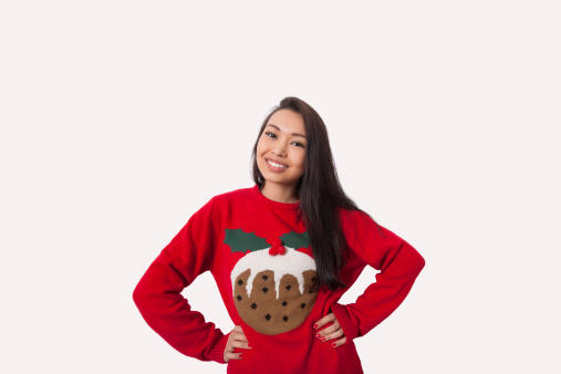 Portrait of woman in Christmas sweater standing with hands on hips over gray background
