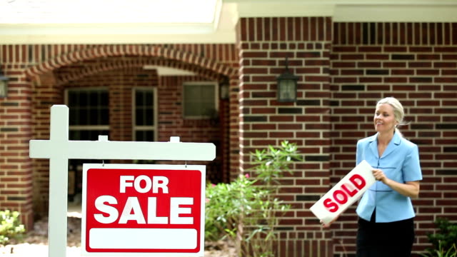 Real estate agent places sold sign on home for sale.