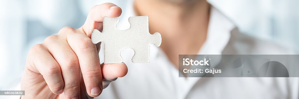 Businessman Holding Jigsaw Puzzle Piece Businessman Holding a Conceptual White Jigsaw Puzzle Piece in Close up Using his Bare Hand. 2015 Stock Photo