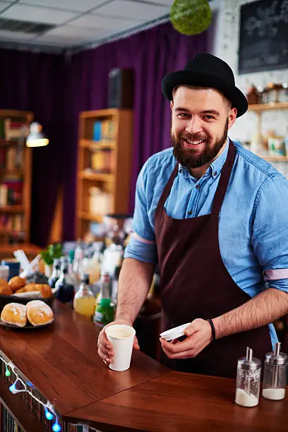 Smiling barista looking at camera and holding disposable cup