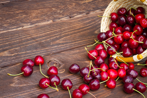 Fresh cherries spilled from a basket on a wooden background with a copy space