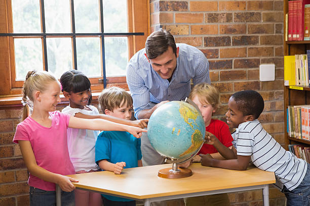istock Cute pupils and teacher looking at globe in library 480369140