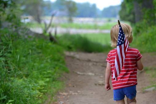Young boy walking down a trail and carrying an American Flag.  