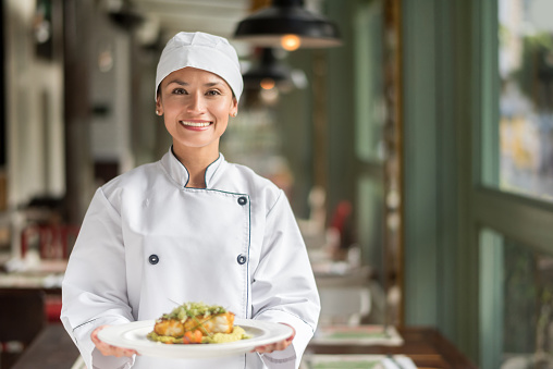 Woman Chef serving a plate at a restaurant and looking very happy smiling to the camera