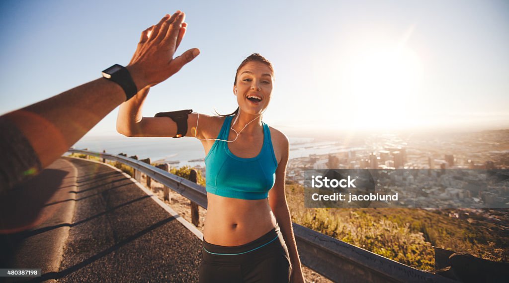 Fit young woman high fiving her boyfriend after a run Fit young woman high fiving her boyfriend after a run. POV shot of runners on country road looking happy outdoors with bright sunlight. Personal Perspective Stock Photo