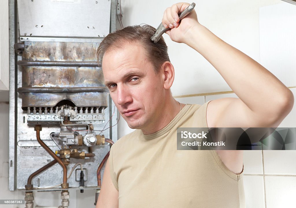 man with  wrench thinks of repair   gas water heater The man with a wrench thinks of repair of a gas water heater 2015 Stock Photo