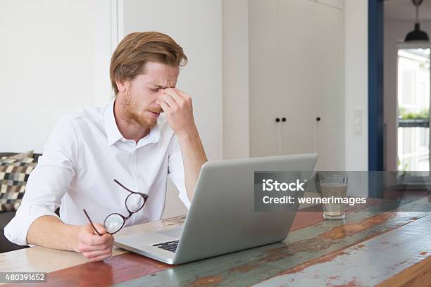 Young Man Sitting With Laptop And A Headache Stock Photo - Download Image Now - 2015, Adult, Apartment