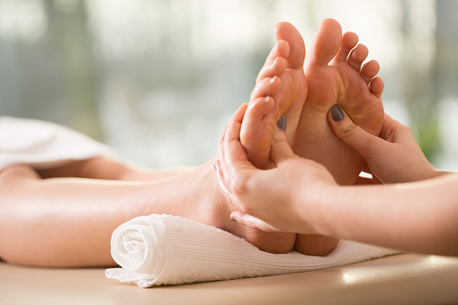 Vertical close-up photo of a masseur applying pressure during a reflexology foot massage in a spa