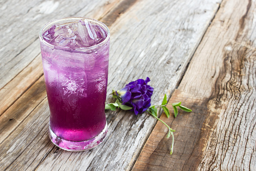 Juice of Butterfly pea with lemon and ice in glass on wooden table. Herb drink for refreshment.