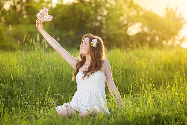 Beautiful woman with flowers in spring sunshine. Girl is holding a lillac on the green meadow.
