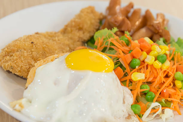 Thai American fusion style fried rice with fried egg and fried chicken served with salad closeup focused on yolk