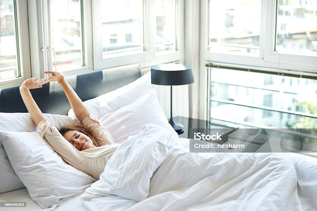 Morning stretch in bed Young woman is doing morning stretching in bed, arms raised, rear view Waking up Stock Photo