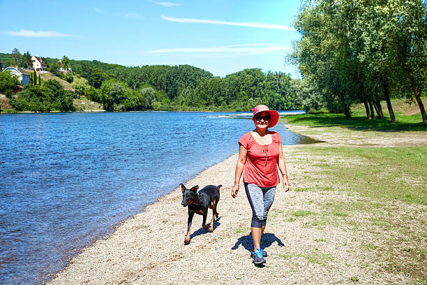 Mature hispanic woman walking dog alongside River Dordogne