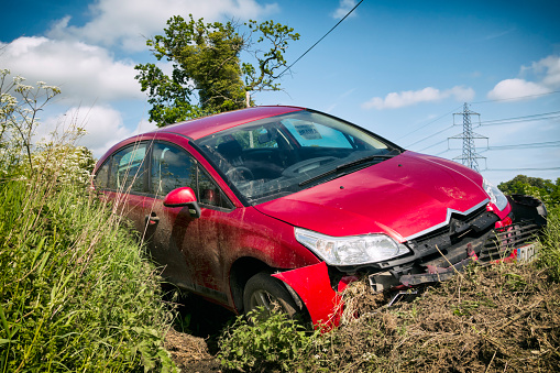 Suffolk, England - May 23, 2015: A red Citroen car crashed into a ditch and damaged. Seen on a rural road in the county of Suffolk, England, on a sunny spring day. The authorities had been made aware of the accident and one window of the car displayed a document to that effect.