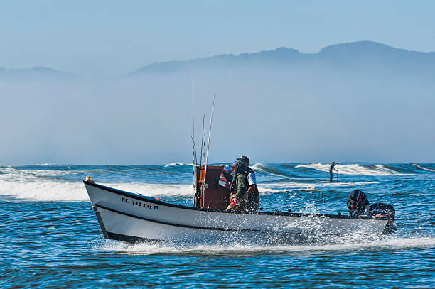 Pacific City, Oregon USA - July 2, 2015: A dory boat crest a wave while a paddle board person pass in the opposite direction.  Dory captians are constantly watching out for obstacles both in the water and on the sandy beach.