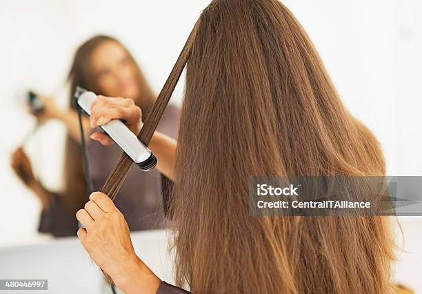 Woman Straightening Hair With Straightener Rear View Stock Photo - Download Image Now