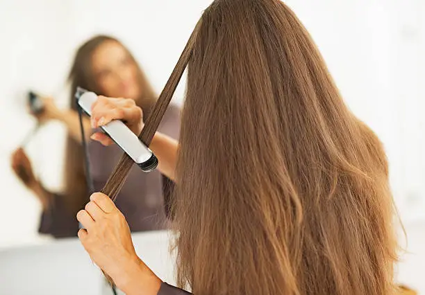 Woman straightening hair with straightener . rear view