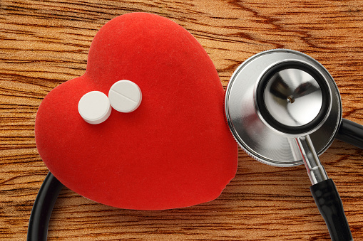 Gray stethoscope and red heart isolated on wooden white background