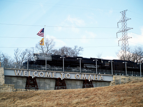 A set of curved railroad tracks slanted toward the inside of the curve atop a gravel railroad bed and railroad ties in a forested area on a sunny day.