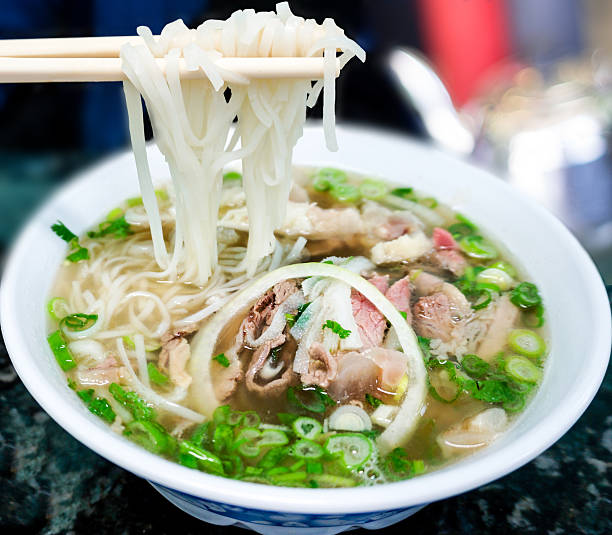 Traditional Vietnamese Pho Beef Noodle Soup Bowl of Vietnamese pho noodle soup with rare beef, tendon, tripe and brisket served with onions, scallions and cilantro. Selective focus and deliberate shallow depth of field on background. vietnamese culture photos stock pictures, royalty-free photos & images